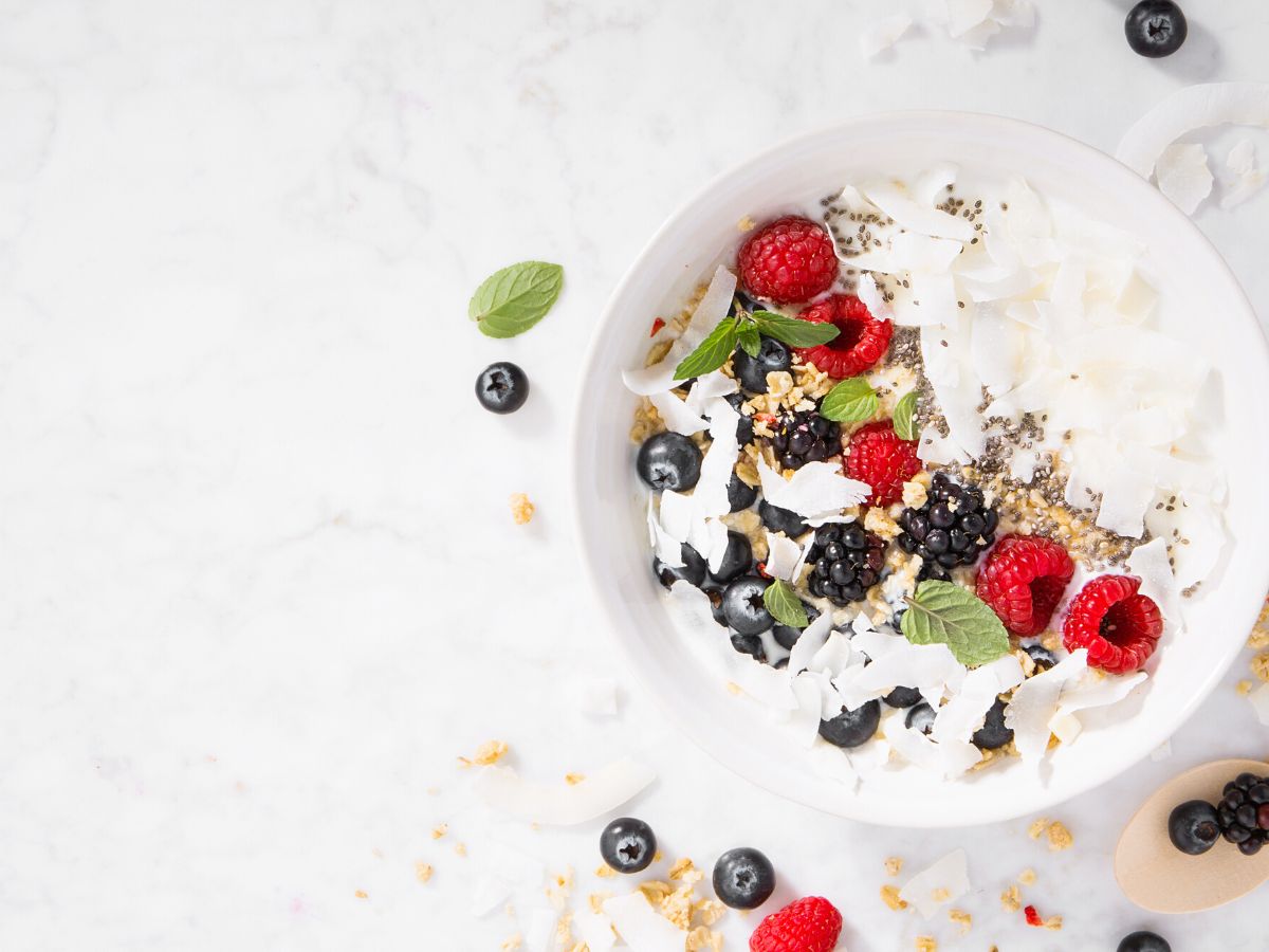 Yogurt bowl on white counter topped with berries, almonds and mint.
