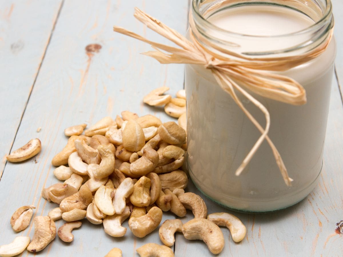 A glass jar filled with cashew cream, with cashews scattered around it.