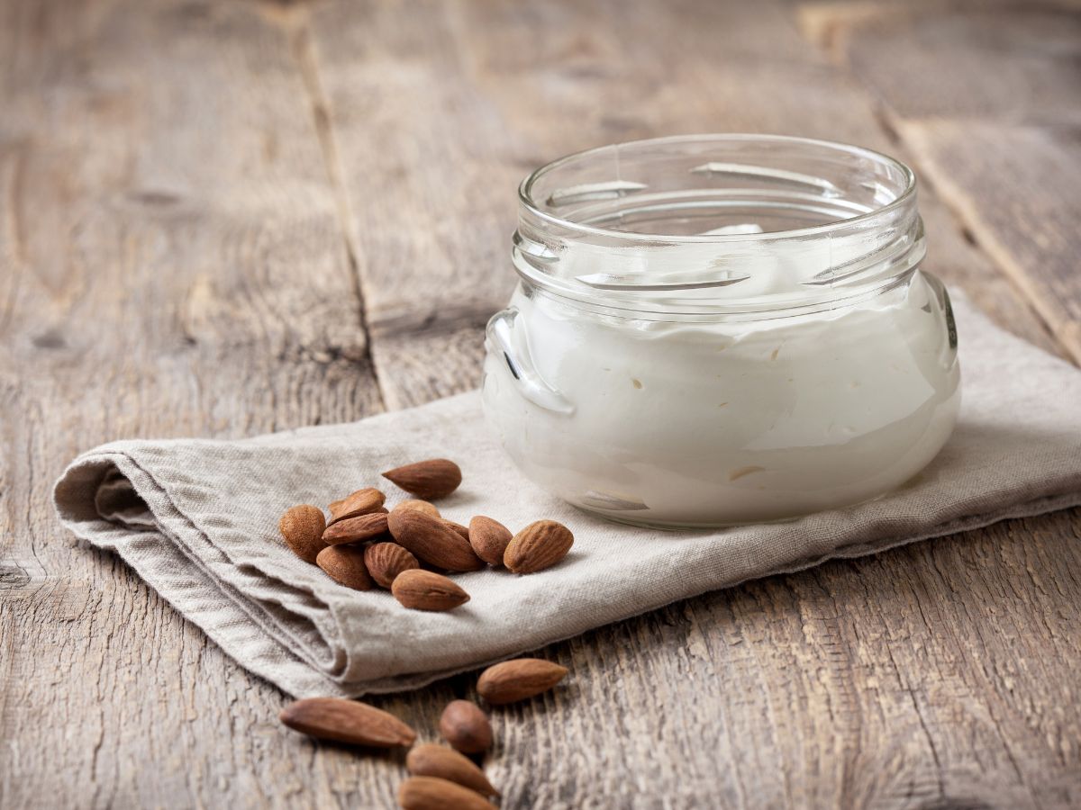 A glass jar with almond yogurt in it, with almonds scattered around it.
